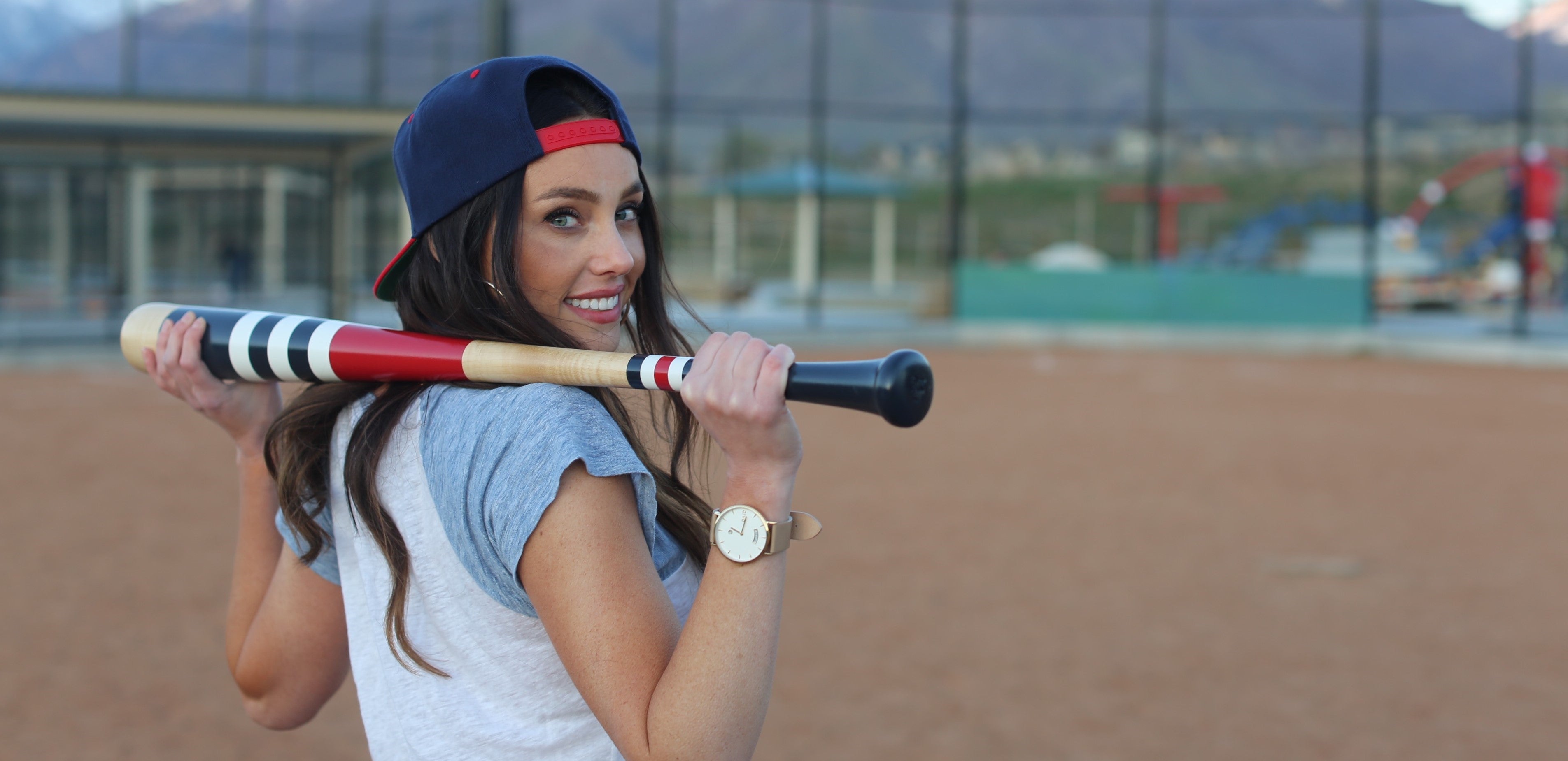 Young woman holding a bat on a softball field. She is wearing an Arvo Awristacrat Watch, Gold with a Nude color watch band.