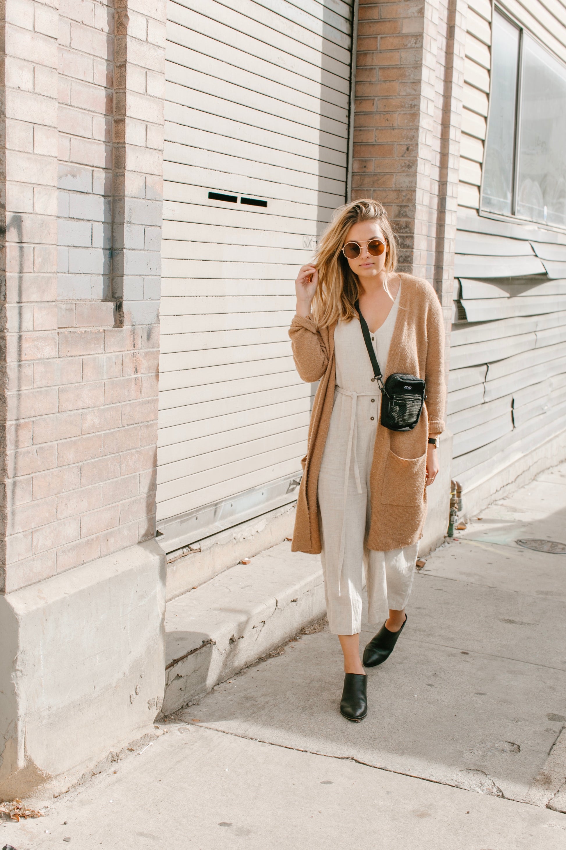 woman walking woman wearing a brown sweater carrying an Arvo Fanny canvas crossbody bags for women in a color named pepper which is black